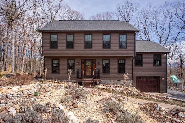 colonial inspired home with an attached garage, a shingled roof, and driveway