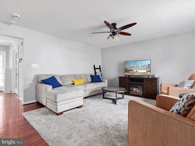 living room featuring a glass covered fireplace, baseboards, wood finished floors, and a ceiling fan