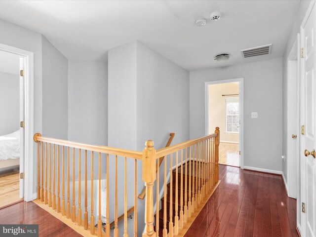 corridor featuring an upstairs landing, visible vents, baseboards, and wood-type flooring