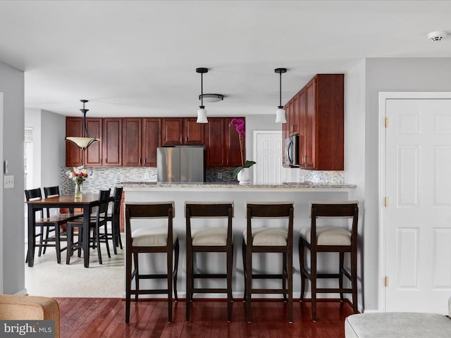 kitchen with backsplash, appliances with stainless steel finishes, a kitchen bar, and a peninsula