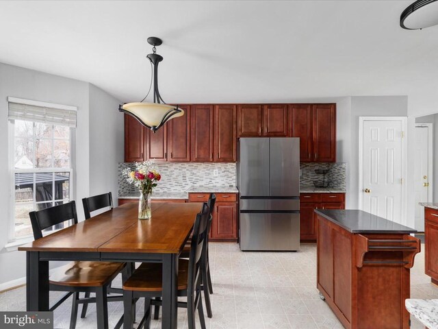 kitchen featuring baseboards, freestanding refrigerator, hanging light fixtures, tasteful backsplash, and reddish brown cabinets