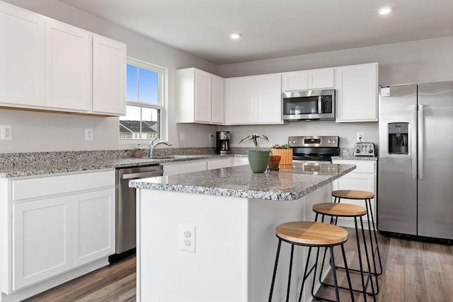 kitchen with a breakfast bar, dark hardwood / wood-style floors, white cabinets, a center island, and stainless steel appliances