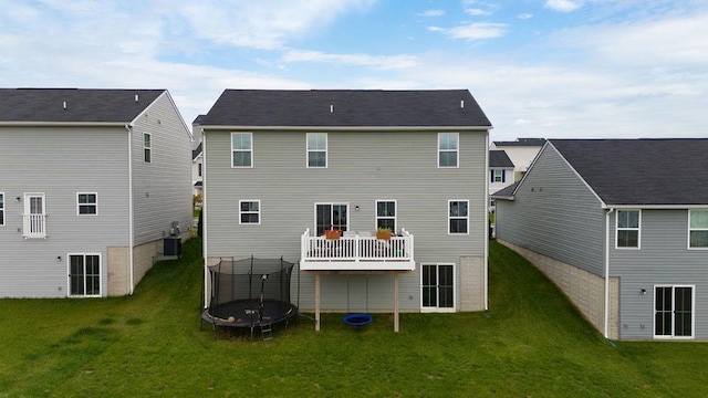 back of house with central AC unit, a yard, and a trampoline