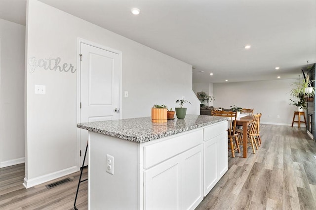 kitchen featuring white cabinetry, a kitchen breakfast bar, a center island, light stone counters, and light hardwood / wood-style floors