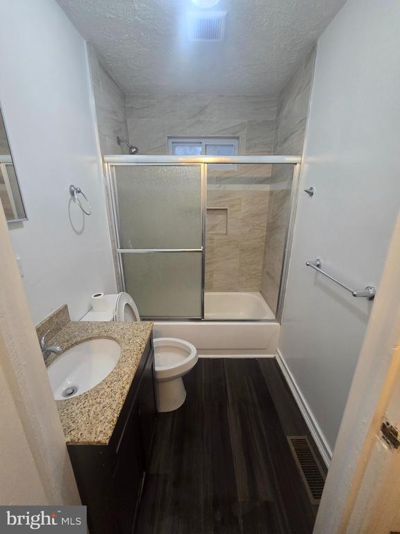 full bathroom featuring enclosed tub / shower combo, hardwood / wood-style floors, vanity, a textured ceiling, and toilet