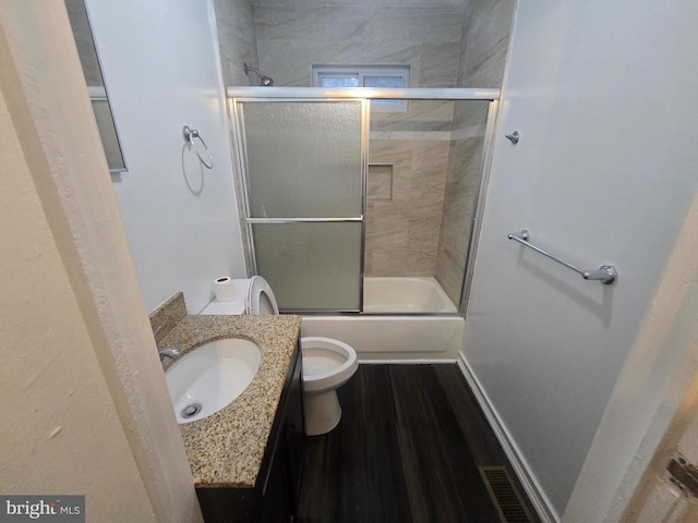 full bathroom featuring hardwood / wood-style flooring, vanity, shower / bath combination with glass door, and toilet