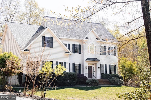 colonial house featuring roof with shingles and a front yard