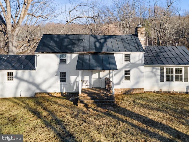 rear view of property featuring a chimney, a yard, metal roof, and a standing seam roof