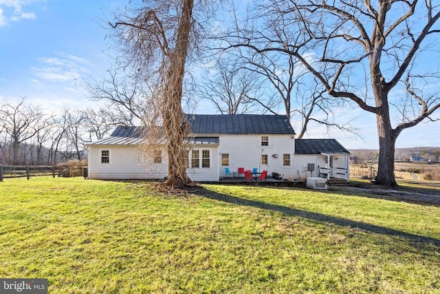 rear view of property with a lawn, a standing seam roof, fence, cooling unit, and metal roof