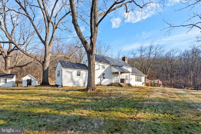 view of home's exterior with a chimney, a storage shed, a yard, metal roof, and a standing seam roof