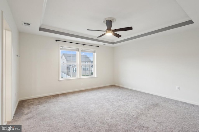 spare room with a tray ceiling, a ceiling fan, visible vents, carpet flooring, and baseboards
