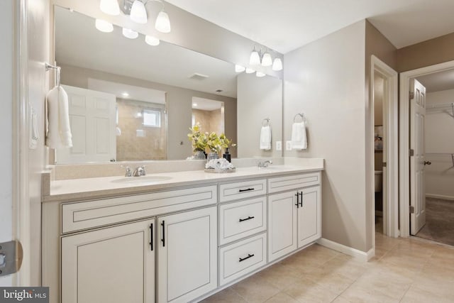 bathroom featuring a tile shower, a sink, tile patterned floors, double vanity, and baseboards