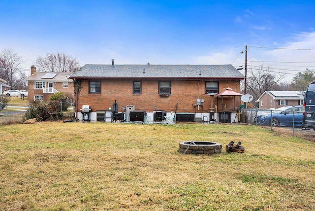 rear view of property featuring a fire pit, brick siding, a lawn, and fence