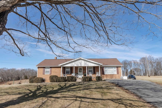 view of front of house featuring a porch, brick siding, driveway, a chimney, and a front yard