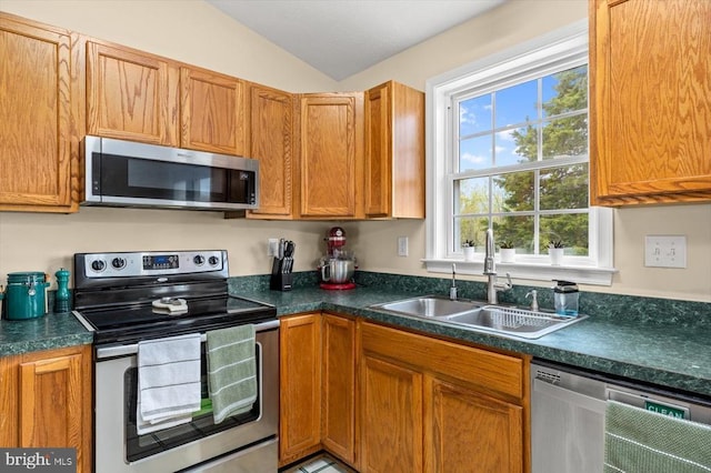 kitchen featuring dark countertops, a sink, lofted ceiling, stainless steel appliances, and brown cabinets