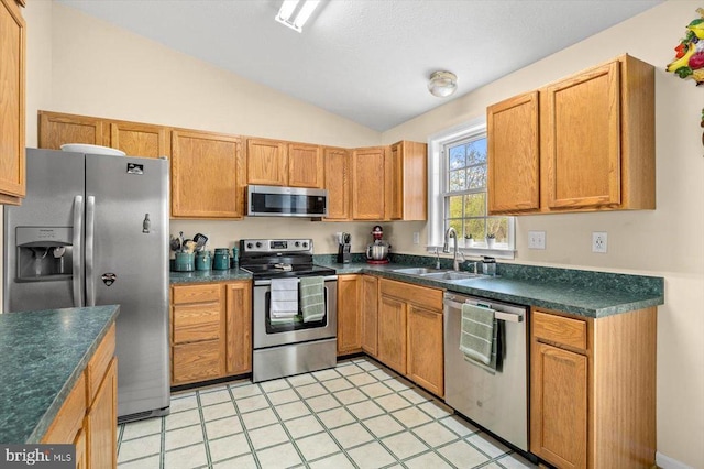 kitchen featuring a sink, dark countertops, appliances with stainless steel finishes, and vaulted ceiling