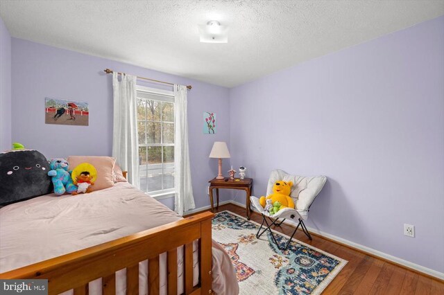bedroom with baseboards, a textured ceiling, and wood finished floors