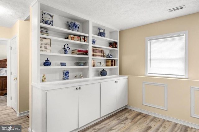 interior space featuring visible vents, a textured ceiling, baseboards, and wood finished floors