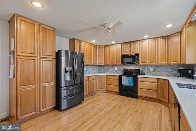 kitchen with black appliances, backsplash, light countertops, and light wood finished floors