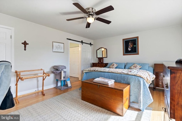 bedroom featuring a barn door, wood finished floors, baseboards, and ceiling fan