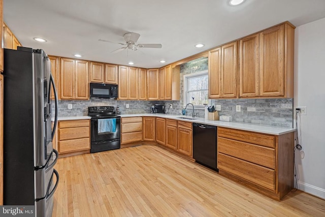 kitchen featuring decorative backsplash, black appliances, light wood-type flooring, and a sink