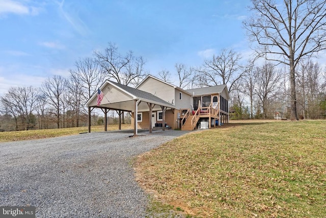 view of front of home featuring an attached carport, gravel driveway, stairs, a front yard, and a sunroom