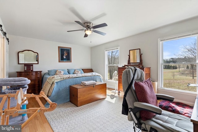 bedroom with ceiling fan, baseboards, a barn door, and wood finished floors