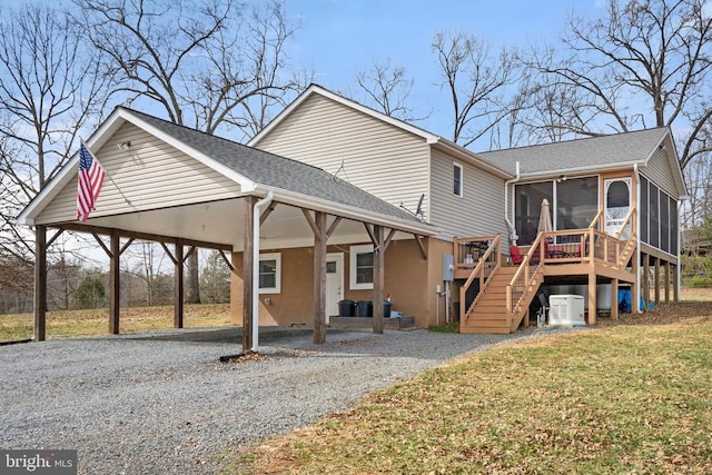 back of house featuring stairway, a lawn, a sunroom, a carport, and driveway