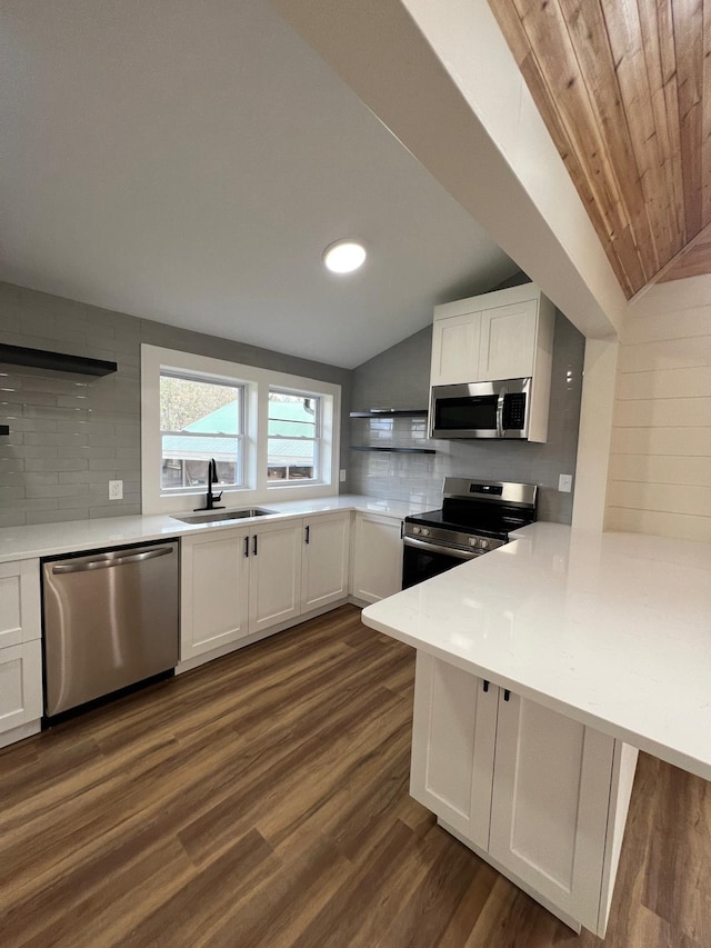 kitchen featuring appliances with stainless steel finishes, white cabinets, dark hardwood / wood-style flooring, vaulted ceiling, and kitchen peninsula