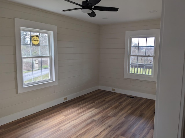 spare room with dark wood-type flooring, wooden walls, and ceiling fan