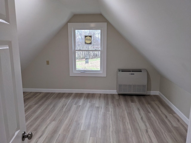 additional living space with vaulted ceiling, heating unit, and light wood-type flooring