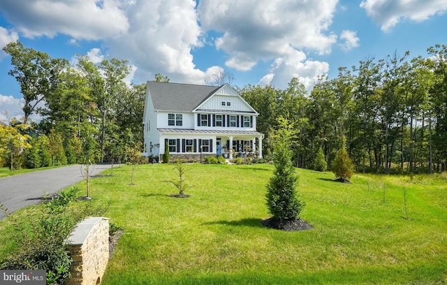 view of front of house with metal roof, aphalt driveway, a standing seam roof, board and batten siding, and a front yard