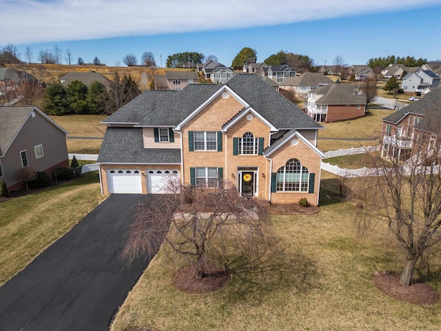 traditional home featuring aphalt driveway, a residential view, a front yard, a garage, and brick siding