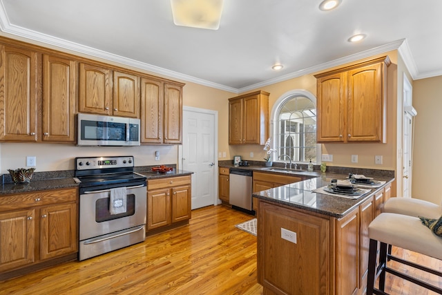 kitchen with a breakfast bar, light wood-style flooring, ornamental molding, a peninsula, and appliances with stainless steel finishes