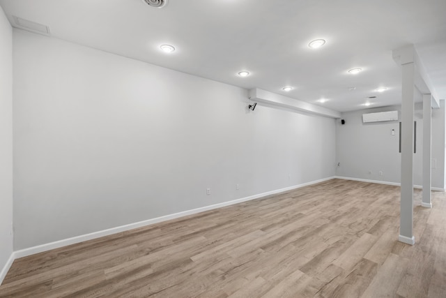 finished below grade area featuring a wall mounted air conditioner, baseboards, light wood-style floors, and recessed lighting