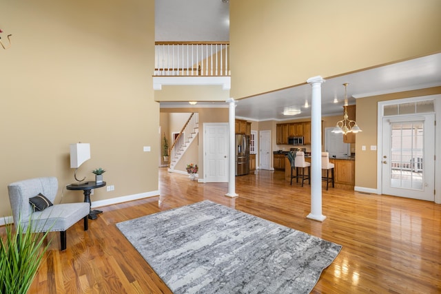 foyer entrance featuring stairway, baseboards, ornate columns, light wood-style floors, and a towering ceiling