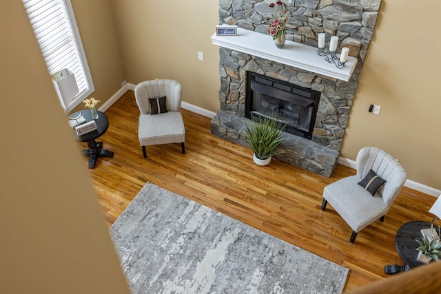 sitting room featuring a stone fireplace, baseboards, and wood finished floors