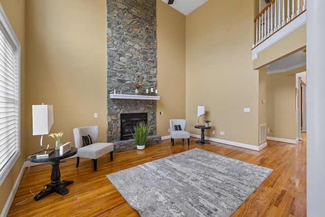 living area featuring visible vents, baseboards, a fireplace, a towering ceiling, and wood finished floors