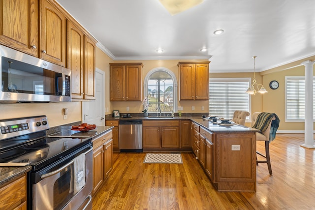 kitchen featuring brown cabinetry, decorative columns, a sink, stainless steel appliances, and a kitchen bar