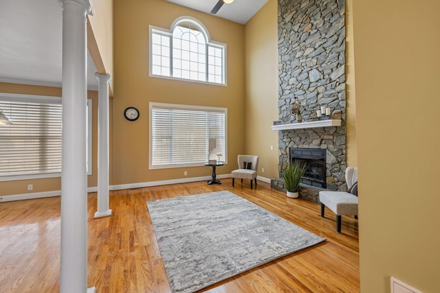 sitting room with a stone fireplace, baseboards, ornate columns, and wood finished floors