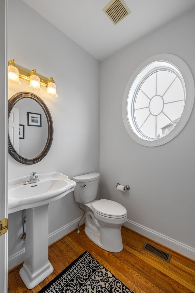 half bath with visible vents, baseboards, toilet, and wood finished floors