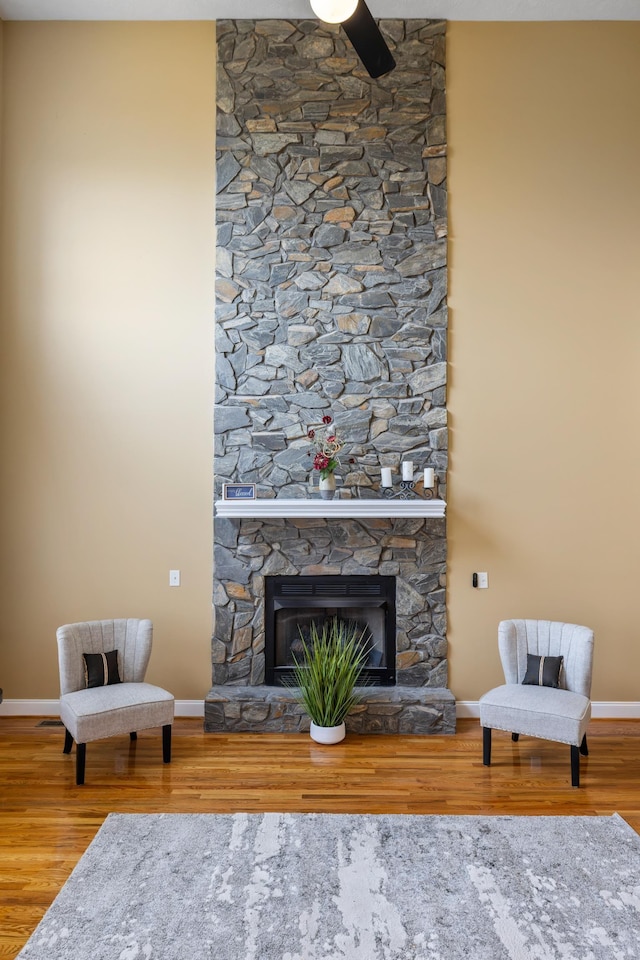 living area with a stone fireplace, baseboards, and wood finished floors