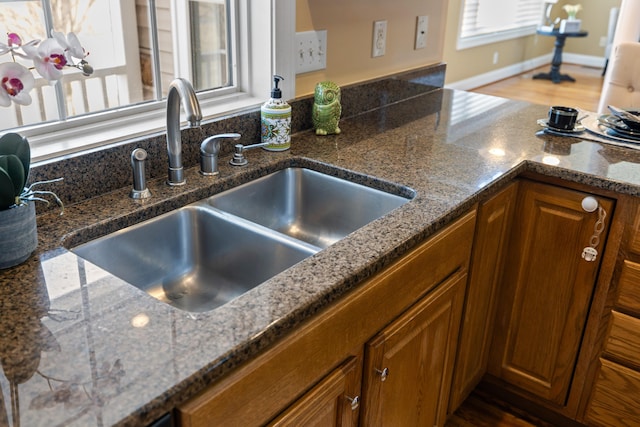 kitchen with dark stone countertops, wood finished floors, baseboards, a sink, and brown cabinets