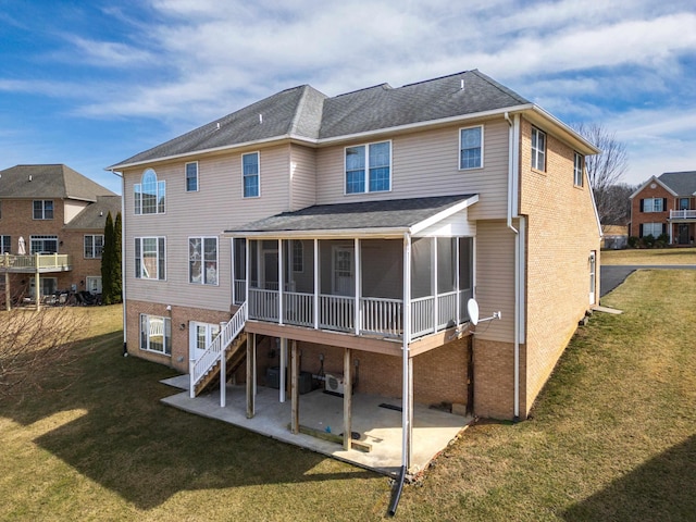 rear view of house featuring brick siding, a patio area, a lawn, and a sunroom