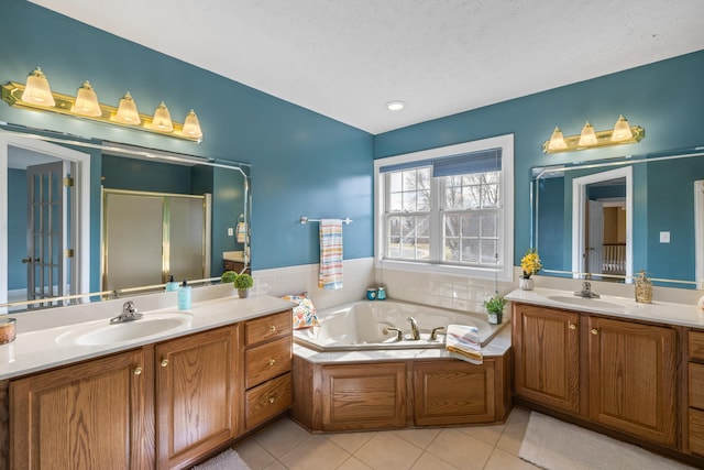 bathroom featuring a tub with jets, a stall shower, two vanities, and a sink