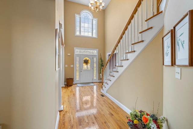 entrance foyer with baseboards, stairs, a high ceiling, an inviting chandelier, and wood finished floors