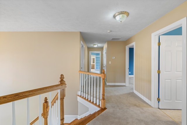 hallway with visible vents, an upstairs landing, light colored carpet, and baseboards