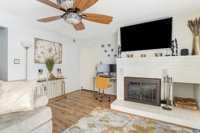 living room featuring visible vents, a ceiling fan, a brick fireplace, wood finished floors, and baseboards