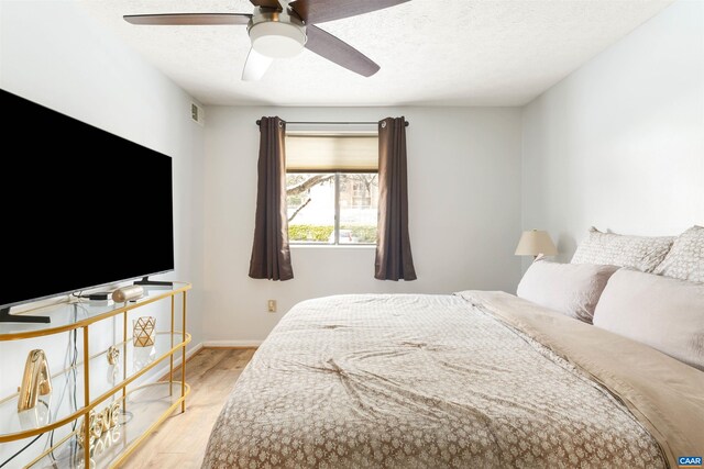 bedroom featuring light wood-type flooring, visible vents, a textured ceiling, and baseboards