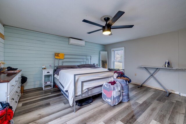 bedroom with hardwood / wood-style flooring, ceiling fan, wood walls, and an AC wall unit